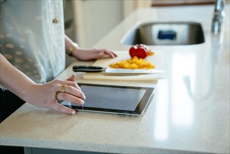 Woman using digital tablet and chopping food in domestic kitchen
