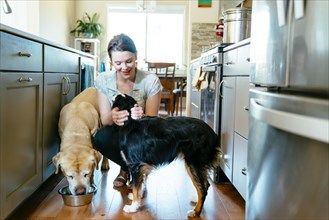 Woman feeding and petting dogs in domestic kitchen