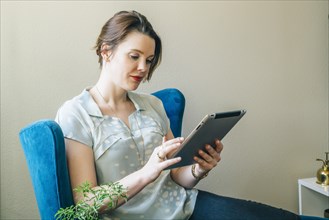 Woman sitting in armchair using digital tablet
