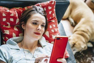 Woman laying on sofa near dog texting on cell phone