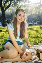 Portrait of smiling Caucasian girl sitting on blanket in park
