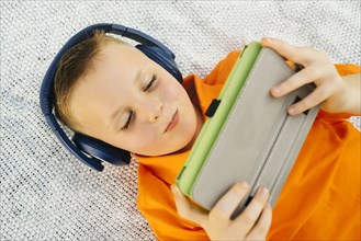 Smiling Caucasian boy laying on blanket listening to digital tablet