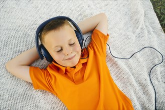 Smiling Caucasian boy laying on blanket in park listening to headphones