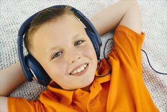 Smiling Caucasian boy laying on blanket in park listening to headphones