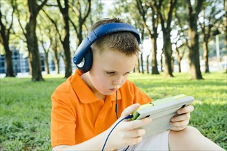 Serious Caucasian boy listening to digital tablet in park