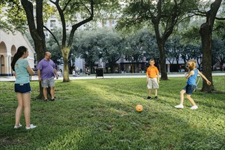 Caucasian family kicking soccer ball in park