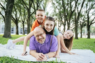 Portrait of Caucasian boy and girls laying on back of father in park