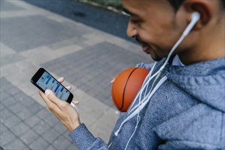 Black man holding basketball listening to cell phone with earbuds