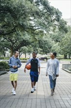 Smiling Black friends walking in park with basketball