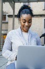 Smiling Black woman using laptop outdoors