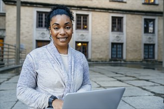Portrait of smiling Black woman using laptop outdoors