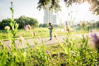 Mixed Race woman standing on running path in park beyond wildflowers