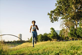 Mixed Race woman running in grass near waterfront