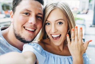 Smiling Caucasian couple posing for selfie with engagement ring