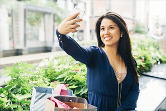 Hispanic woman sitting on bench posing for cell phone selfie