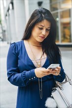 Close up of Hispanic woman texting on cell phone in city