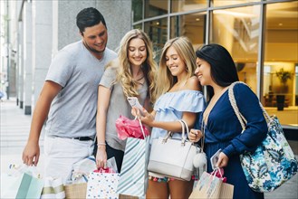 Friends with shopping bags texting on cell phone in city