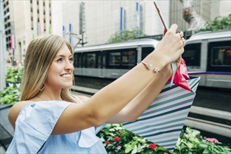 Caucasian woman with shopping bag posing for cell phone selfie
