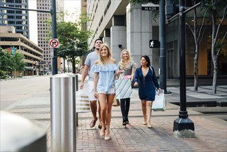 Friends crossing street in city carrying shopping bags