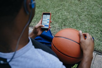Black man listening to cell phone with earbuds and holding basketball