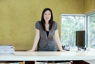 Asian businesswoman leaning on desk