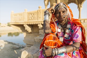 Indian woman wearing traditional jewelry sitting near monument