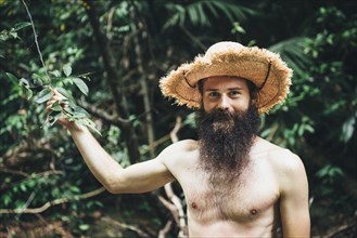 Caucasian man with bare chest holding branch in forest