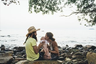 Caucasian mother and father holding baby daughter on rocky beach