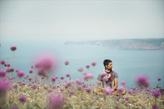 Caucasian man sitting in field of flowers near ocean