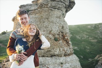 Caucasian couple hugging near rock with bouquet of flowers