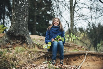Smiling Caucasian woman sitting on tree root holding branch