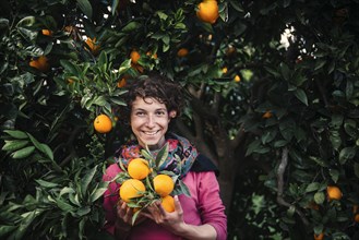 Smiling Caucasian woman holding oranges under tree