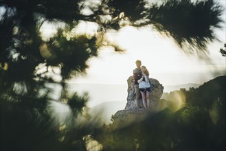 Tree branches framing Caucasian couple hugging at rock