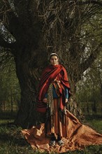 Caucasian woman wearing traditional clothing standing near tree