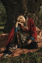 Caucasian woman wearing traditional clothing sitting near tree