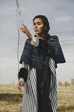 Caucasian woman wearing traditional clothing examining twig