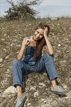Caucasian woman wearing overalls sitting in rocky field