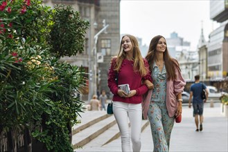 Smiling Caucasian women walking arm in arm in city