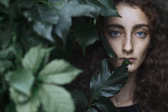 Portrait of serious Caucasian woman behind leaves