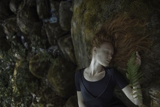 Caucasian woman with red hair laying on rock
