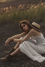 Sexy Caucasian woman wearing white dress sitting in field