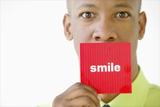Portrait of businessman holding "smile" sign over mouth