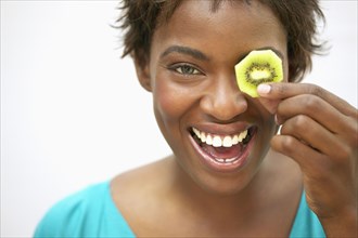 Woman holding kiwi slice in front of eye