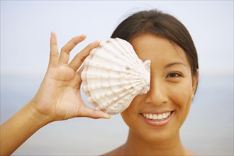Asian woman holding seashell over eye
