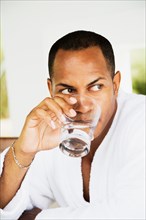 Mixed race man in bathrobe drinking water