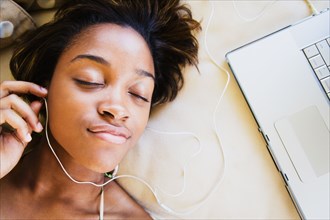 African woman listening to music on headphones connected to laptop