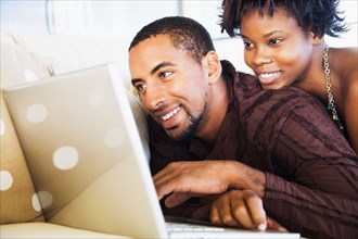 African couple using laptop on sofa