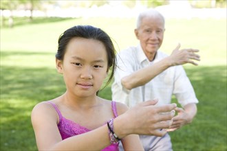 Senior Chinese grandfather and granddaughter doing tai chi outdoors