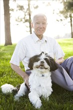 Senior Chinese man sitting in grass with Shih Tzu dog