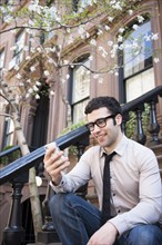 Hispanic businessman using cell phone on front steps